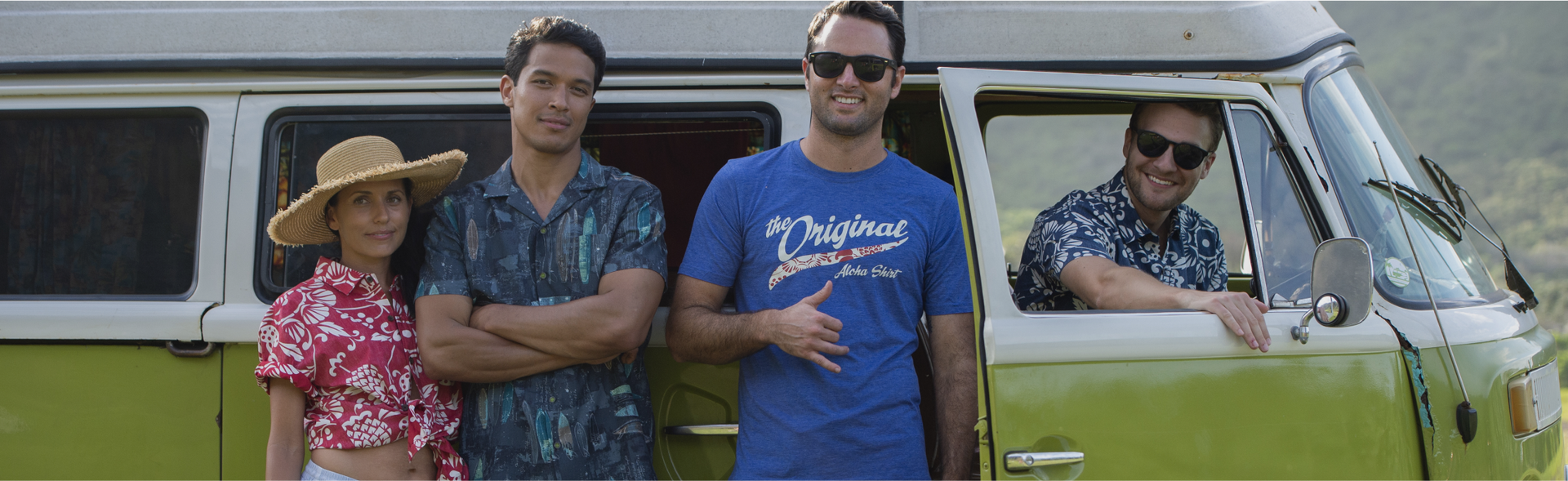 two men and a woman standing leaning back on a green retro looking car with a man looking out the window. They are all wearing Kahala apparel.